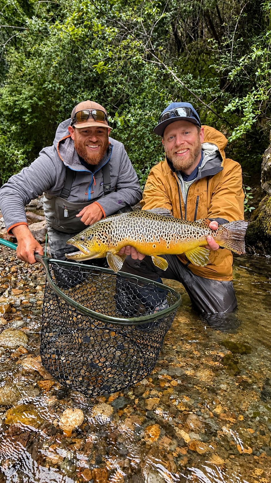 Two anglers with a brown trout and a landing net on a rocky stream