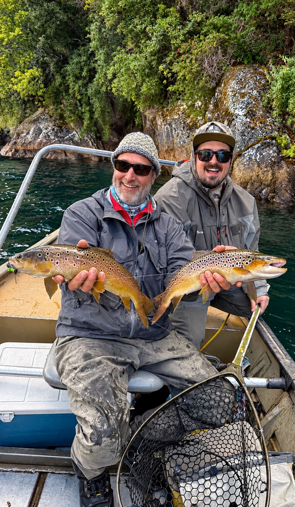 Two anglers with a brown trout aboard the boat