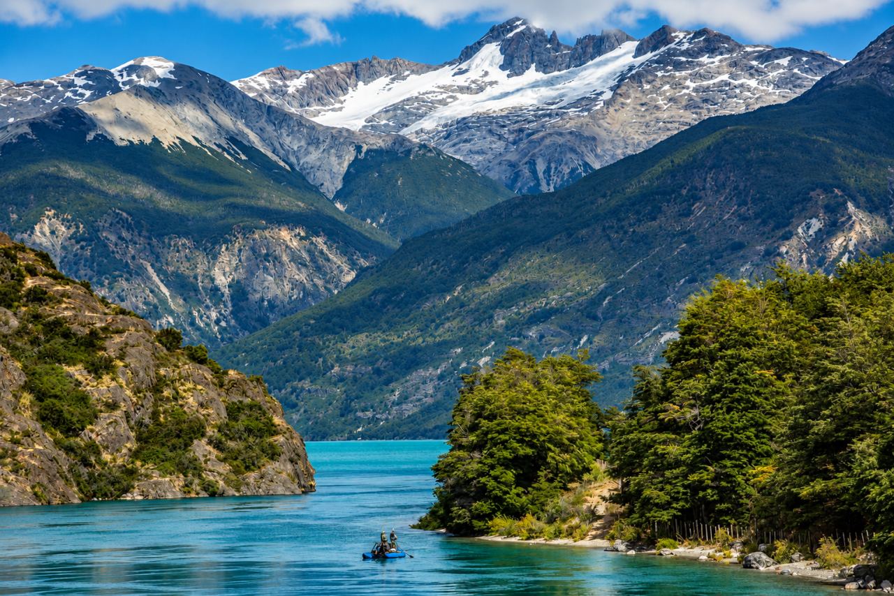 A boat on a turquoise lake beneath snow-capped mountains