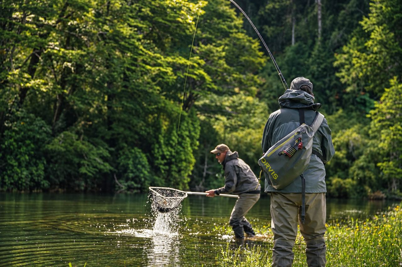 Guide netting a trout for an angler on a wilderness river